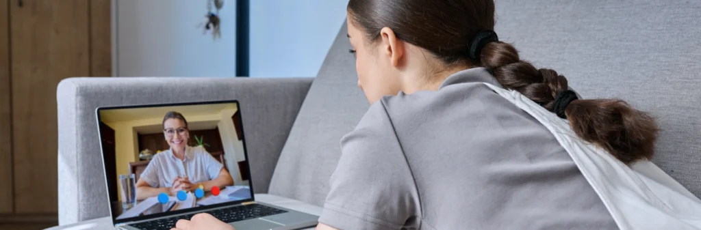 Image of a woman sitting on her sofa, attending a telehealth therapy session from her laptop - How Telehealth Services Are Changing Addiction Treatment - Shanti Recovery and Wellness