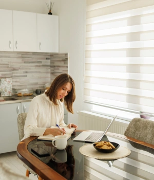 Image of a woman sitting at her kitchen table with her laptop and attending a peaceful virtual recovery session