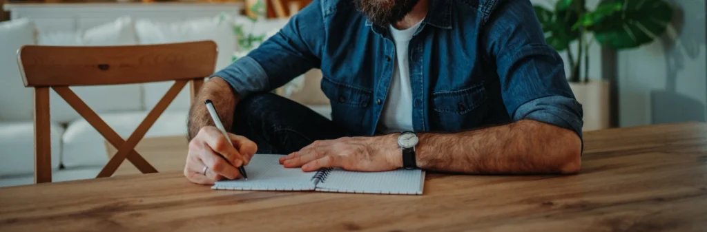 Image of a man sitting at a table writing in his journal - Relapse Prevention Planning Worksheet - Shanti Recovery and Wellness